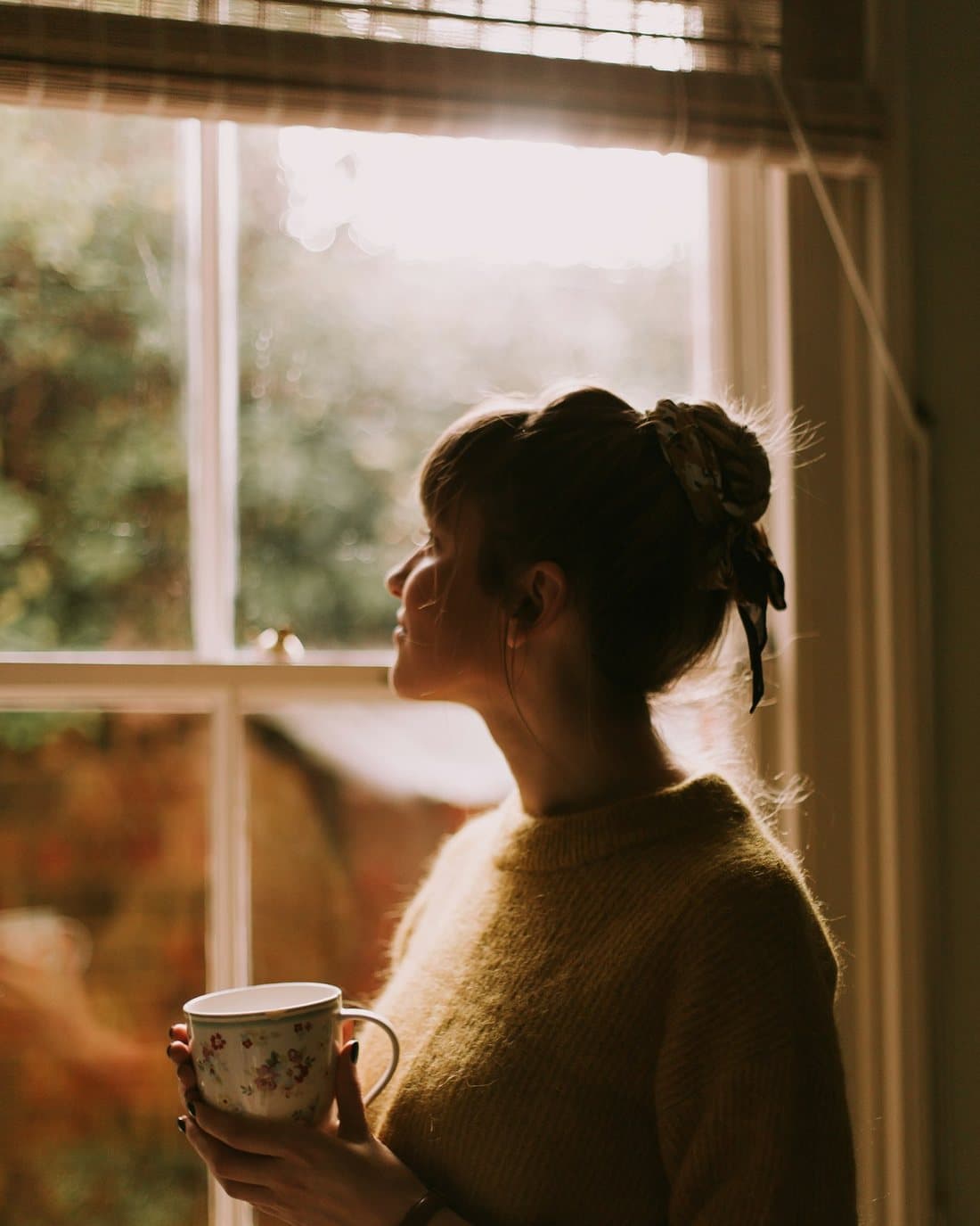 A woman resting calmly by a window with a warm drink, representing relief from anxiety